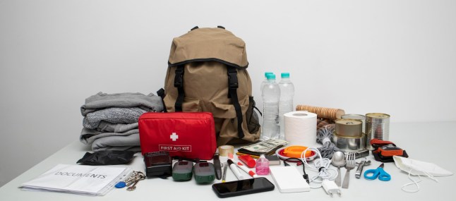 Emergency backpack equipment organized on the table. Documents, water,food, first aid kit and another items needed to survive.; Shutterstock ID 2180383547; purchase_order: -; job: -; client: -; other: -