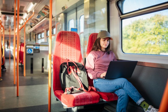 Female college student using laptop in the train on the way to class.