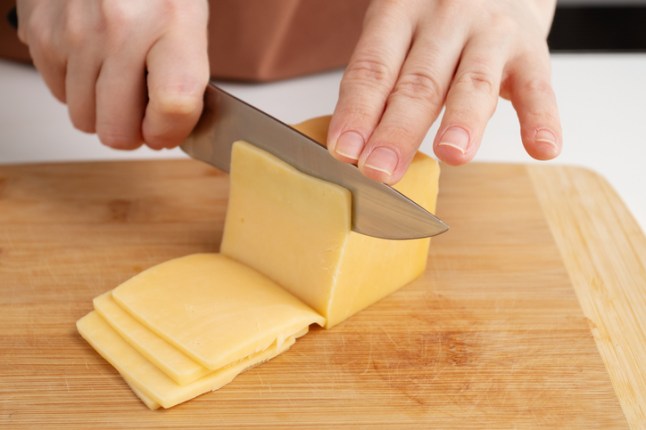 Woman cutting a piece of cheese in the kitchen, slicing it for breakfast meal.