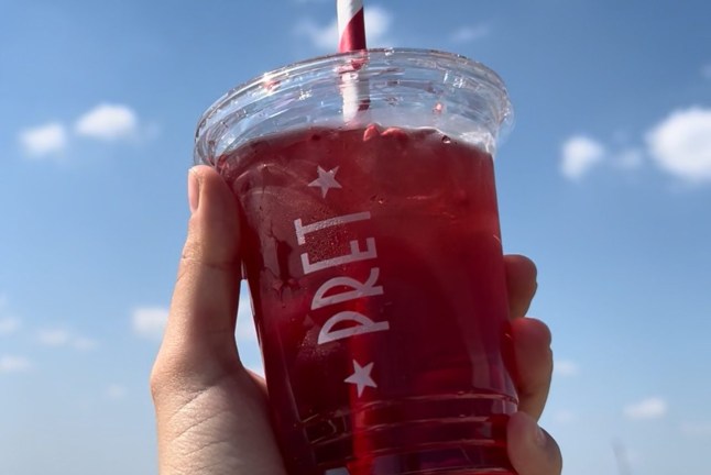 A hand holding a Pret Raspberry Cooler up with the sky in the background
