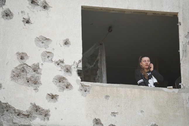 A woman looks though the window of her damaged apartment following a Russian strike in Kharkiv, Ukraine